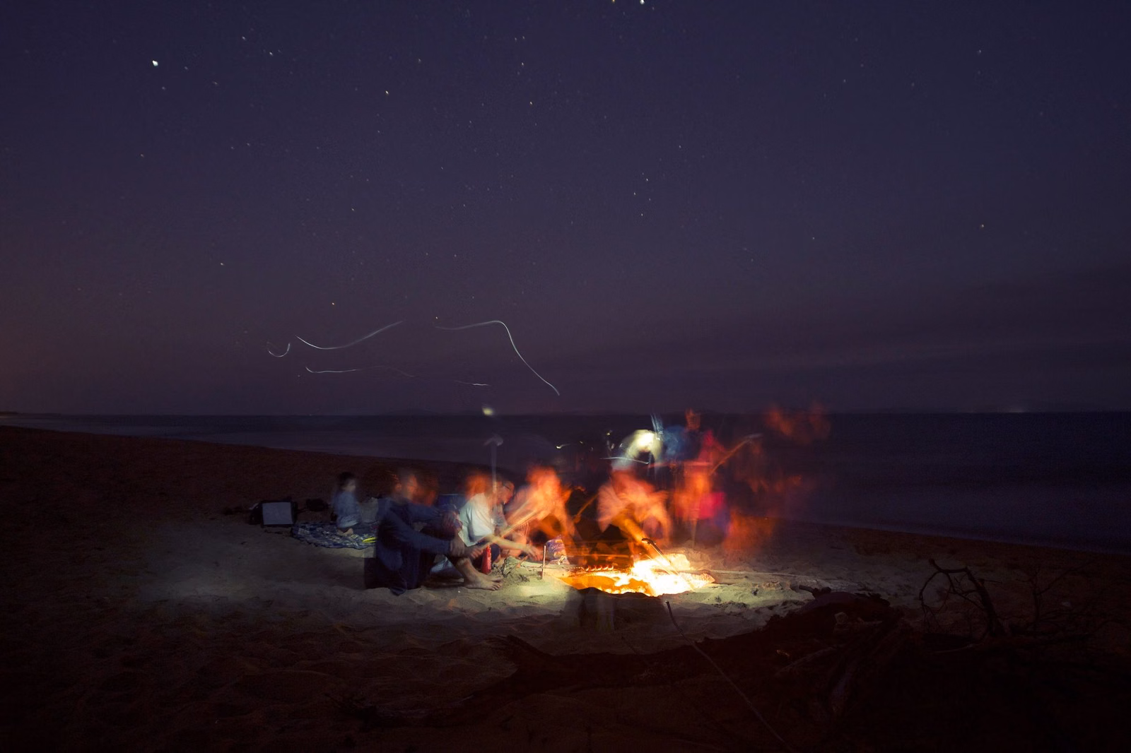 A group gathered around a beach bonfire at night on the Southern California coast