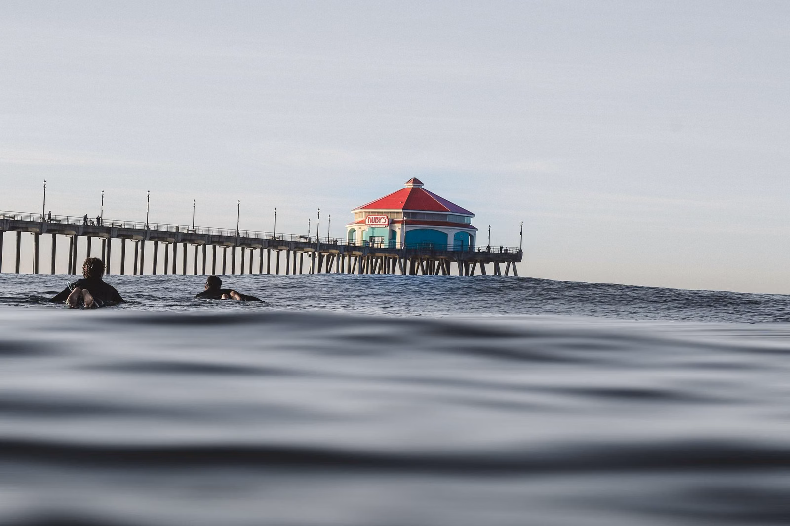 Swimmers in calm water with the Huntington Beach Pier in the distance