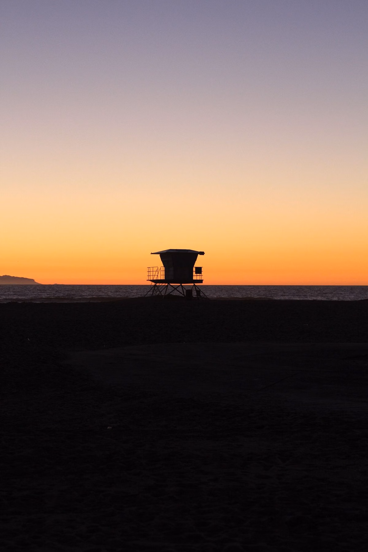 A lifeguard tower silhouetted against an orange evening sky at Huntington Beach