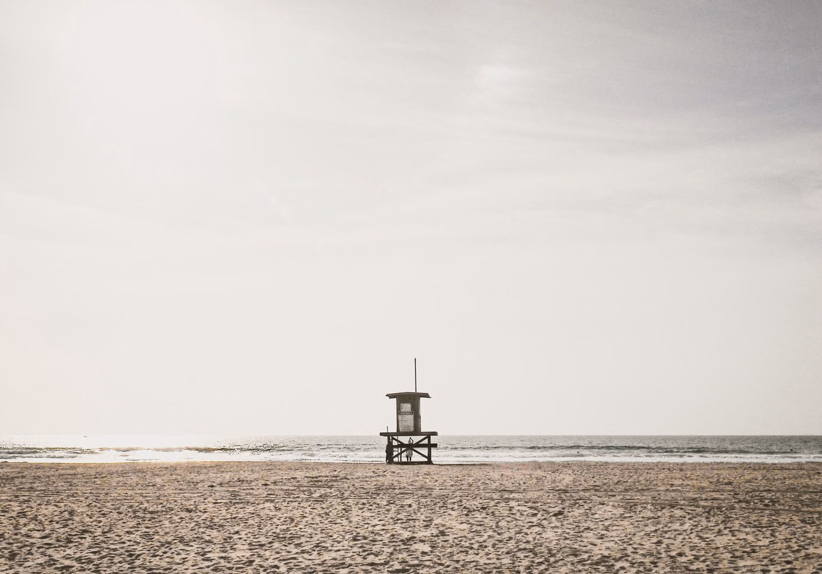 A gray, hazy morning on a wide sandy beach with an empty lifeguard tower near the water